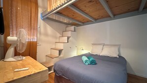 Un dormitorio con cama, ventilador, escritorio de madera y una escalera.