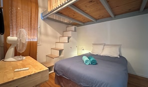 Ein Schlafzimmer mit einem Bett, einem Ventilator, einem Holztisch und einer Treppe.