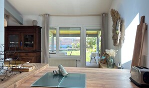 Ein Zimmer mit einem Holztisch, einer Matte, einem Schrank, einem Fenster und Blick ins Freie.