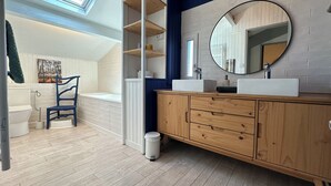 Un baño moderno con tragaluz, tocador de madera, bañera blanca y una silla azul.