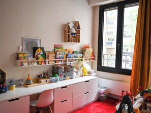 A child's room with a desk, shelves with books and toys, a window with curtains, and a red carpet. - Nice 85 M² Decorated With Nice Terrace With Trees (Paris)