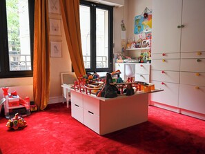Un espace de jeux pour enfants avec un bureau, des jouets et une fenêtre avec des rideaux.