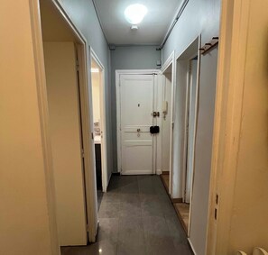 A narrow hallway with a white door at the end, a light fixture on the ceiling, and a wooden floor. - Apartment for 4 people with Wifi in Paris (Paris)