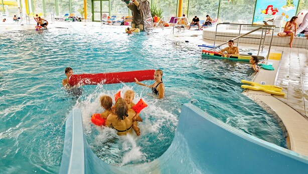 An indoor swimming pool with multiple lanes, a lifeguard stand, and a poolside area with lounge chairs. - Vacation rental for 4 people, right on the Osserbad in Lam in the Bavarian Forest (Lam)