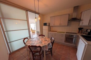 A kitchen with a dining table, chairs, cabinets, a microwave, and a stove. - Beautiful city center apartment with terrace (Jard-sur-Mer)