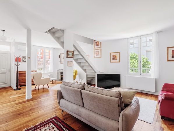 A spacious living area with a sofa, a red chair, a TV, and a staircase.