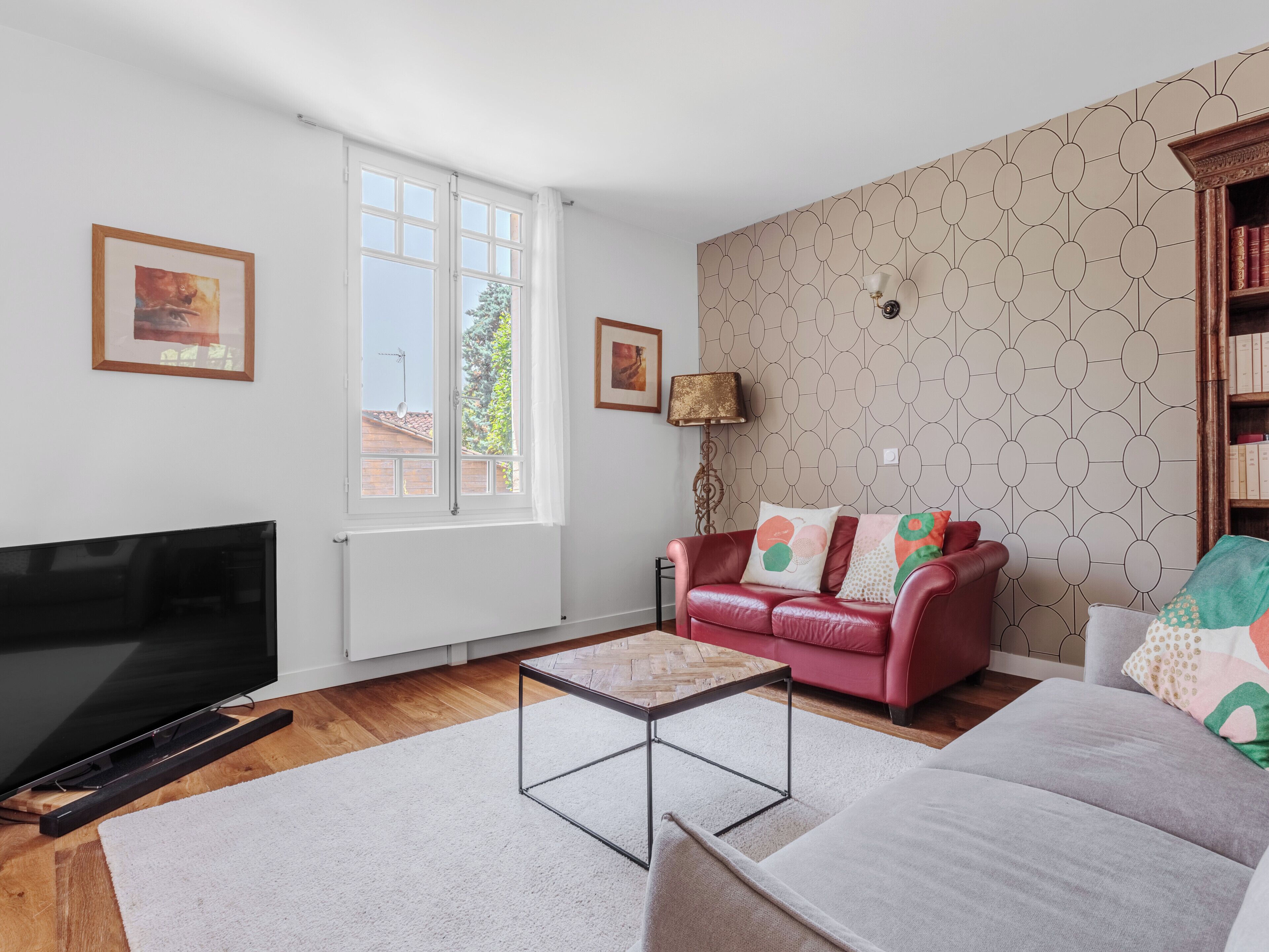 A living room with a TV, a red sofa, a patterned wall, and a bookshelf.