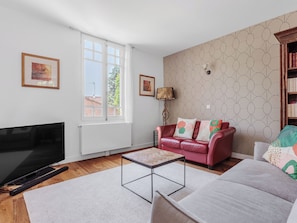 A living room with a TV, a red sofa, a patterned wall, and a bookshelf.