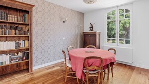 Un comedor con una estantería de madera, una mesa con mantel rosa y vistas al exterior.