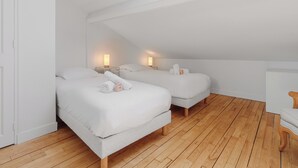 Un dormitorio moderno con decoración en blanco, dos camas, suelo de madera y un tragaluz.