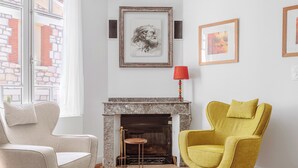Una sala de estar con chimenea, dos sillones y cuadros en la pared.