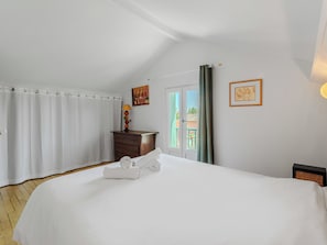 A bedroom with a large bed, a wooden dresser, a door with a view, and a painting on the wall.