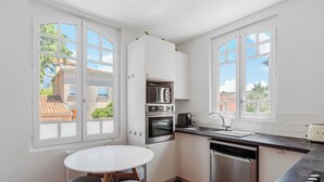 Una cocina moderna con armarios blancos, una mesa redonda para comer con dos taburetes grises y un lavavajillas.