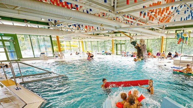 An indoor swimming pool with multiple lanes, a lifeguard stand, and a poolside area with lounge chairs. - Vacation rental for 2 people, right on the Osserbad in Lam in the Bavarian Forest (Lam)