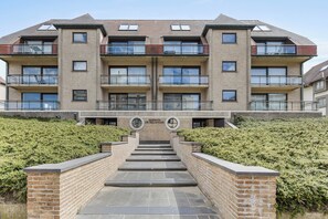 A multi-story residential building with balconies, a central entrance with steps, and a sign indicating the name of the building. - 2 bedroom accommodation in Oostduinkerke (Oostduinkerke)