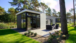 Een modern huis met een glazen patio, tuinmeubilair en een verzorgde tuin.