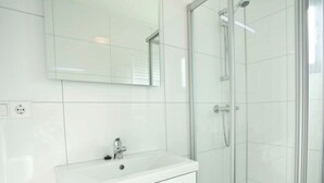Een moderne badkamer met een witte wastafel, spiegel en douche met glazen wanden.