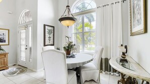 A dining area with a round table, white chairs, a hanging light fixture, and a view through a large window. - Private Pool, Wifi, Outdoor Lounger, Family Fun (Rotonda West)