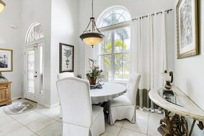 A dining area with a round table, white chairs, a hanging light fixture, and a view through a large window. - Private Pool, Wifi, Outdoor Lounger, Family Fun (Rotonda West)