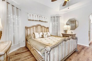 Une chambre à coucher avec un grand lit, une commode en bois, un miroir et un ventilateur de plafond.
