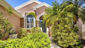 A house with a pink facade, a large window, and a well-maintained garden with various plants. - Private Pool, Wifi, Outdoor Lounger, Family Fun (Rotonda West)