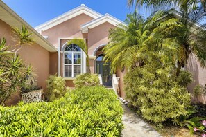 A house with a pink facade, a large window, and a well-maintained garden with various plants. - Private Pool, Wifi, Outdoor Lounger, Family Fun (Rotonda West)