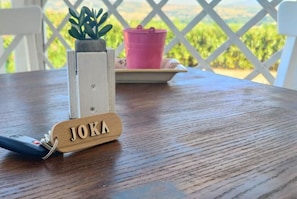 Een houten sleutelhanger met de tekst 'JOKA', een kleine potplant en een roze emmer op een tafel.