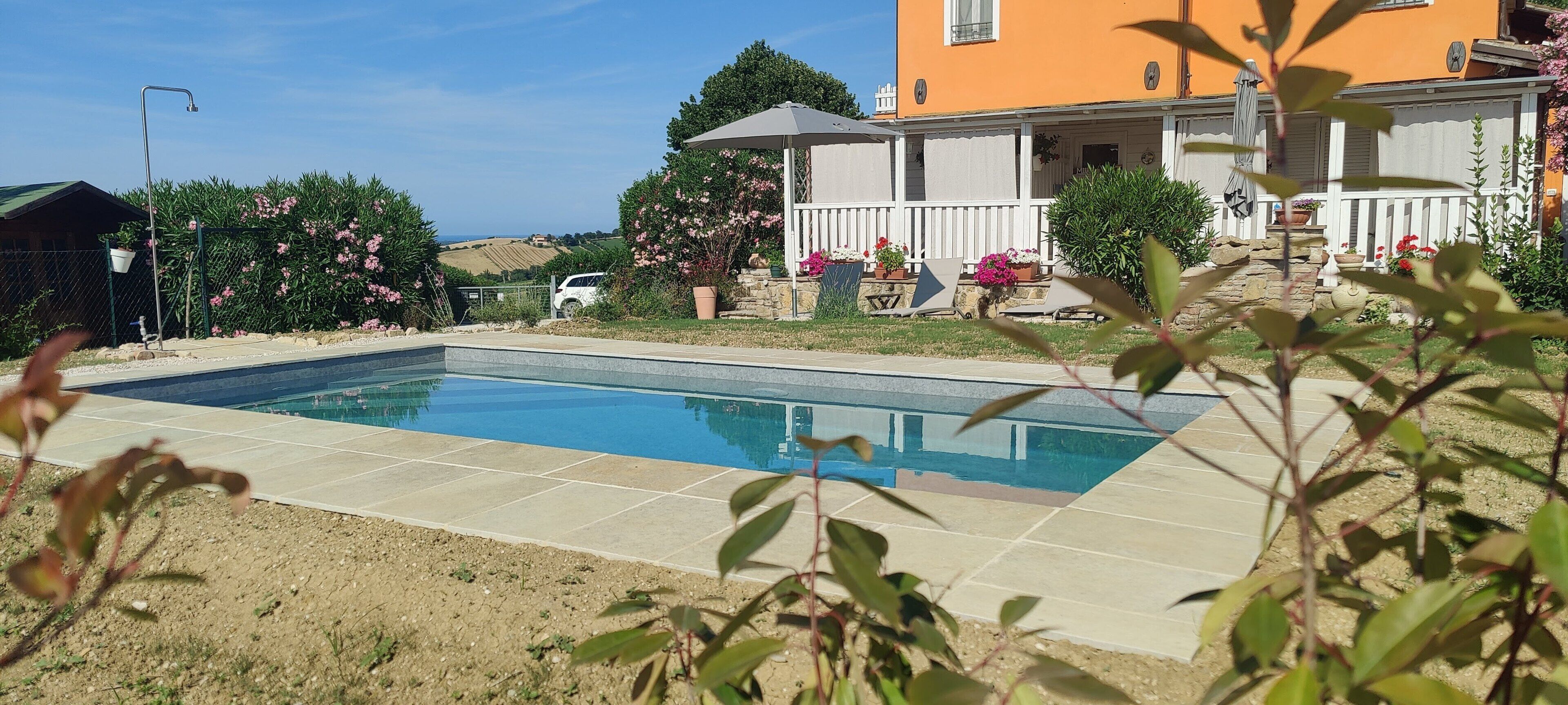 A swimming pool with a tiled deck, surrounded by a garden with various plants and flowers, and a building with a white fence and a balcony.