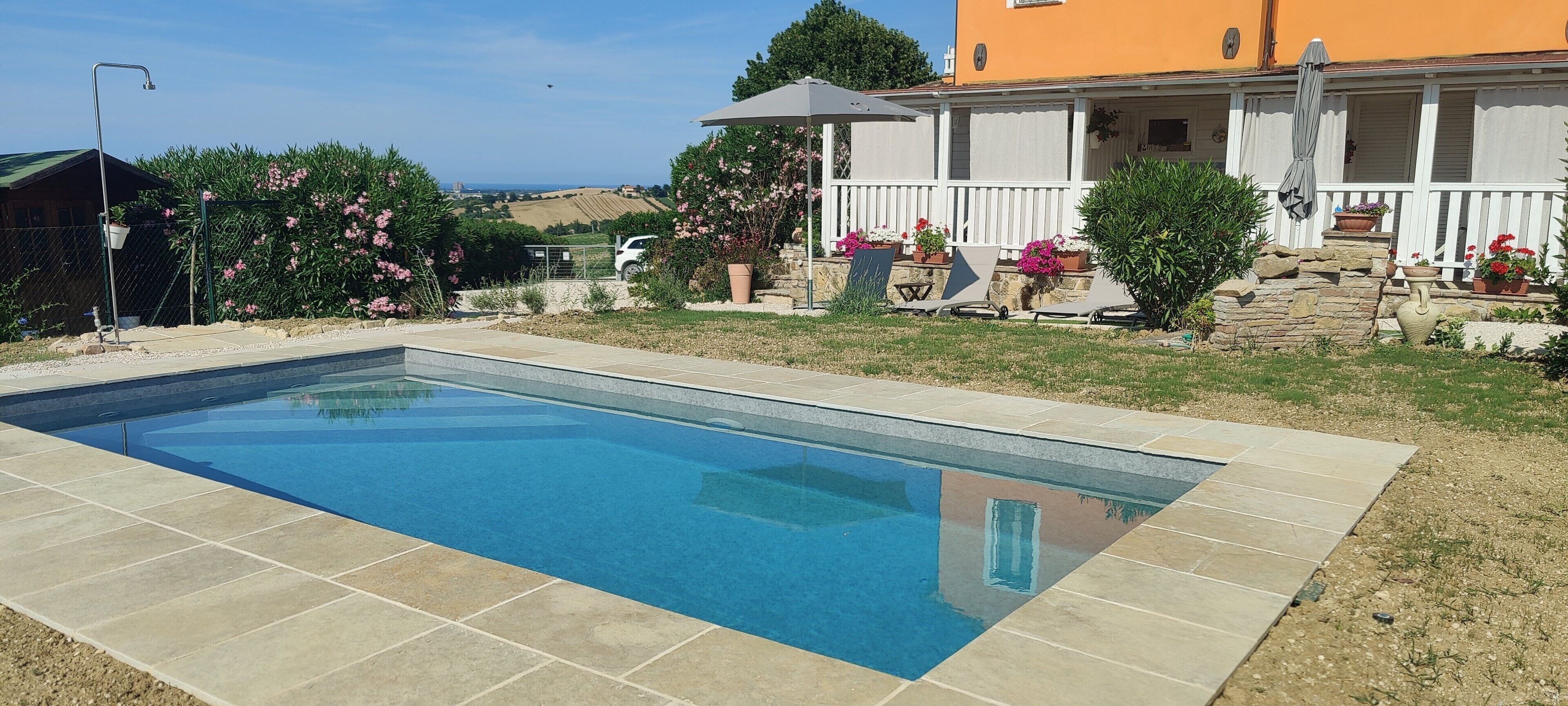 A rectangular swimming pool with a tiled edge, surrounded by a grassy area with potted plants and a white fence.