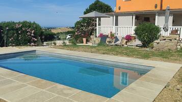 Une piscine rectangulaire dont le bord est recouvert de carreaux, entourée d’une pelouse agrémentée de plantes en pot et d’une clôture blanche.