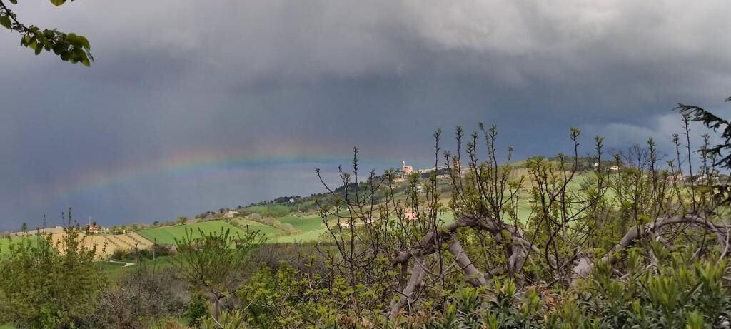 A landscape with a rainbow, a hill, and some buildings in the distance.
