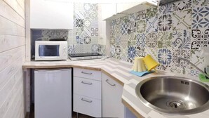 Una cocina compacta con microondas, un refrigerador pequeño, un lavamanos y azulejos estampados en el salpicadero.