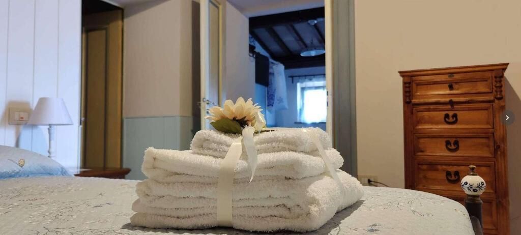 Ein ordentlich bezogenes Bett mit einem Stapel Handtüchern und einer Zierblume, ein Holzkoffer und eine Tür zu einem anderen Raum.