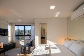 Quarto de hotel moderno com uma cama grande, uma escrivaninha, uma cadeira e uma televisão.