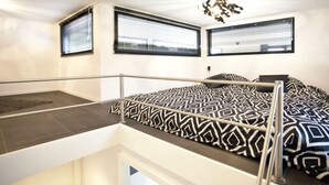Une chambre moderne avec un lit superposé, deux fenêtres équipées de stores, un luminaire au plafond et un petit balcon.