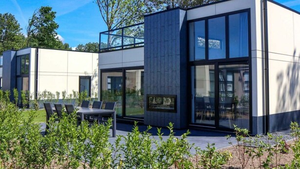 Un bâtiment moderne à deux étages, doté de grandes fenêtres, d’un balcon et d’un espace extérieur aménagé pour s’asseoir.