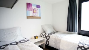 Une chambre d’hôtel avec deux lits, une petite table, une table de chevet, un tableau au mur et une fenêtre avec des rideaux.