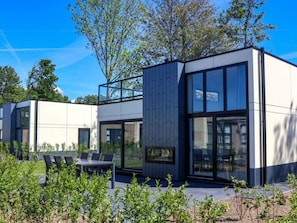 Ein modernes, zweistöckiges Haus mit großen Fenstern, einem Balkon und Sitzgelegenheiten im Freien.