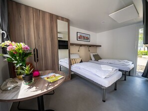 Een moderne hotelkamer met een houten kast, een bureau met een bloevas, twee bedden en een groot raam.