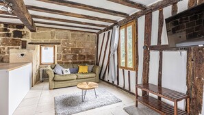 Ein Zimmer mit freiliegenden Holzbalken, Steinwänden, einer Couch, einem kleinen runden Tisch und einem Fernseher.