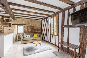 Une pièce avec des poutres apparentes, des murs en pierre, un canapé, une petite table ronde et un téléviseur.
