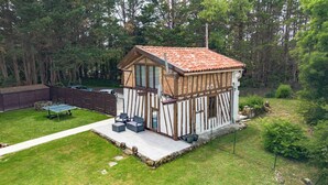 Ein kleines, zweistöckiges Holzhaus mit einem Ziegeldach, einer Terrasse mit Gartenmöbeln und einem umzäunten Garten.