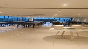 A spacious indoor area with tables and chairs arranged for dining, large windows providing natural light, and a modern design. - Firefox Hotel and Resorts (Hyderabad)