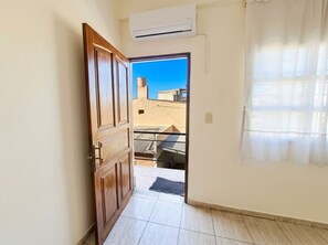 Un couloir menant à un balcon d’où l’on peut admirer les bâtiments environnants, ainsi qu’une unité de climatisation et une porte.