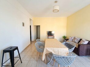 Un espace repas comprenant une table, des chaises, un téléviseur et un canapé avec des coussins.