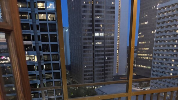 Un balcón con vistas a edificios urbanos, una silla y una puerta.