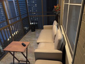 Un balcon avec un canapé, une petite table, un haut-parleur et un vase rempli de fleurs.