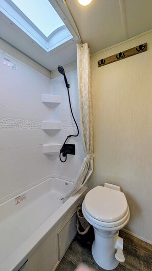 A compact bathroom with a skylight, a shower, a toilet, and a towel rack. - Cozy riverside camper in peaceful Townsend with AC (Townsend)