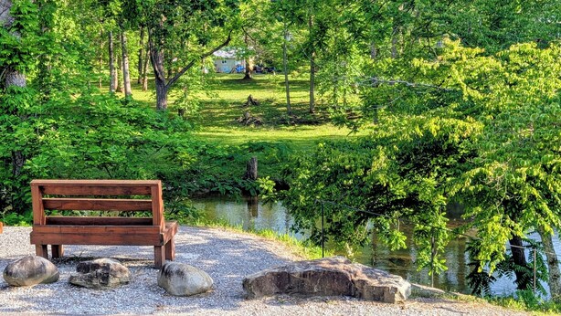 A wooden bench by a pond with rocks, surrounded by lush greenery and trees. - Cozy riverside camper in peaceful Townsend with AC (Townsend)