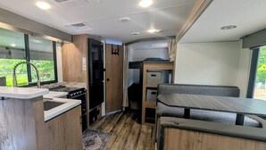 A compact RV interior with a kitchenette, a dining area, and a sleeping berth. - Cozy riverside camper in peaceful Townsend with AC (Townsend)